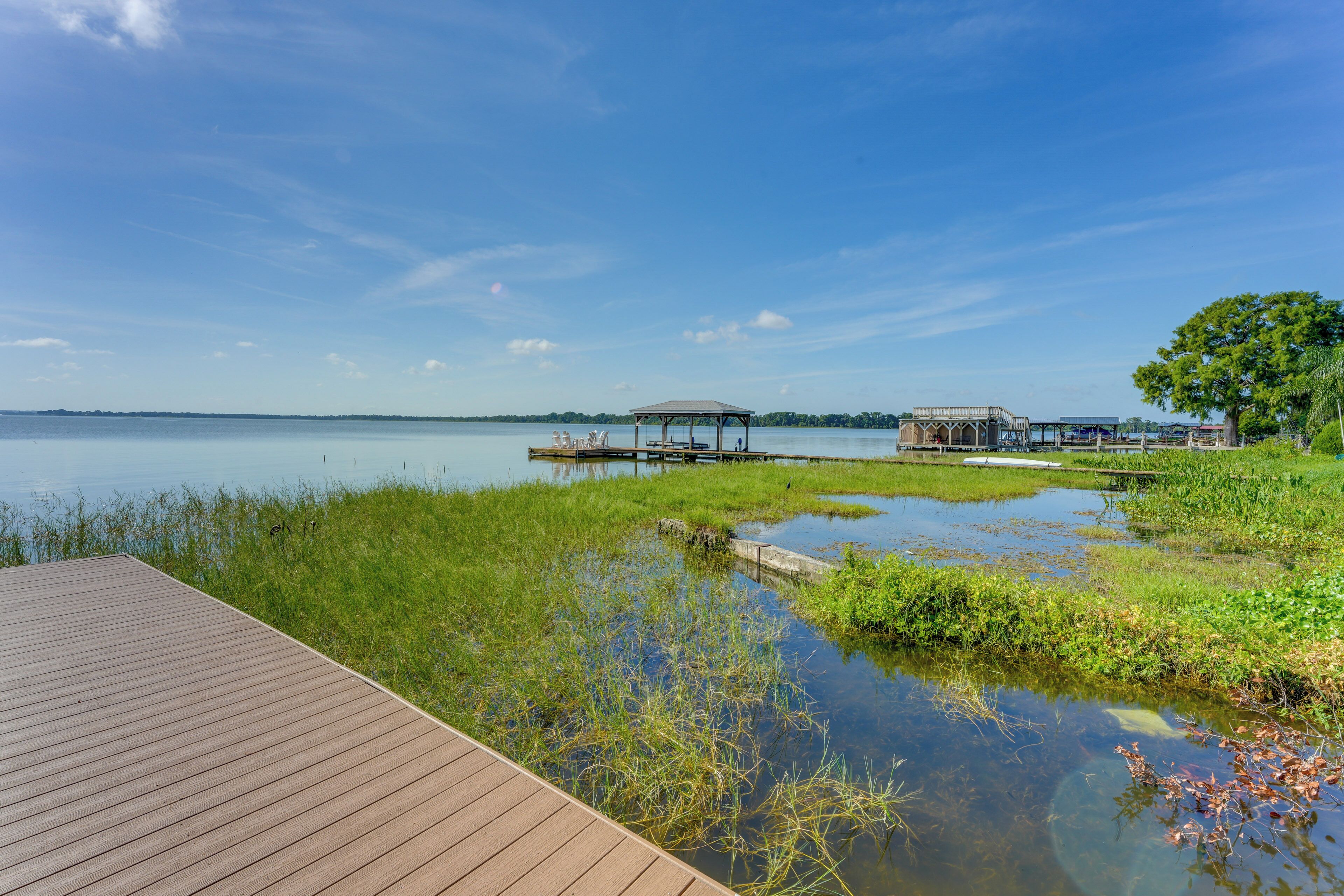 A wooden deck leading to a calm lake with grassy areas and a gazebo.