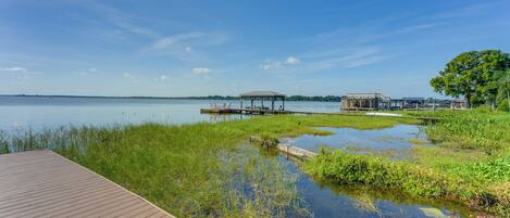 A wooden deck leading to a calm lake with grassy areas and a gazebo.