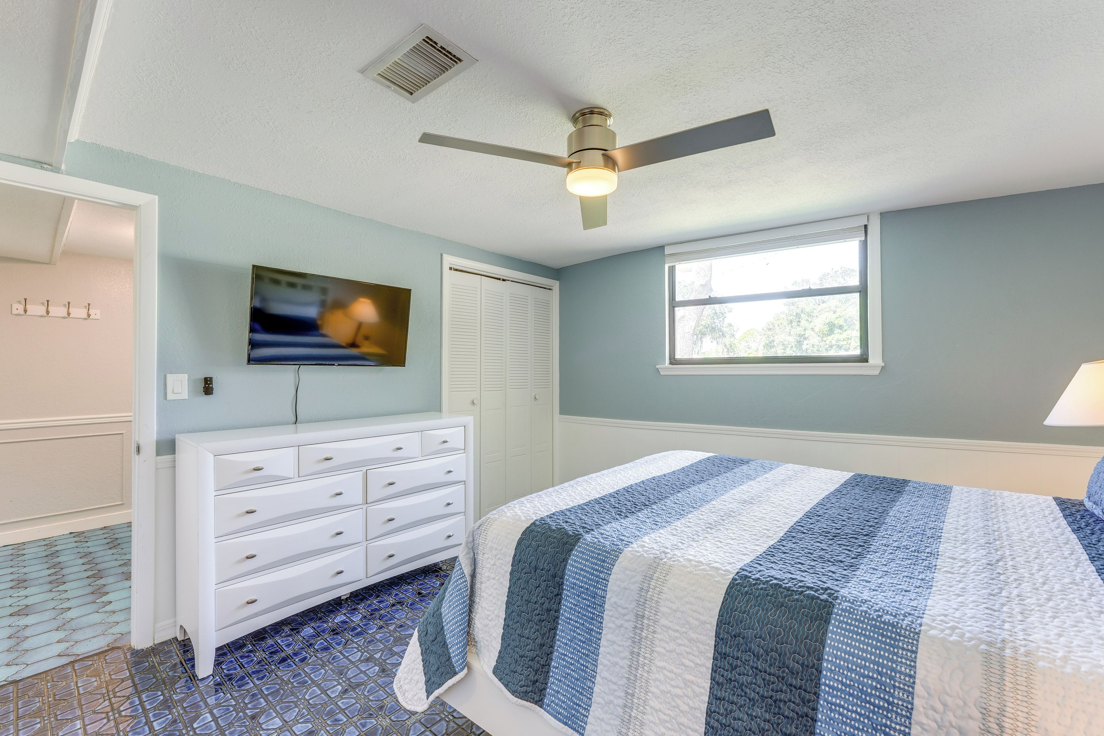 A bedroom with a bed, a dresser, a ceiling fan, a TV, and a window.
