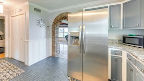 A kitchen with a stainless steel refrigerator, granite countertop, and white cabinetry. - Lake Dora Escape: Canal Access & Seaplane Sights! (Tavares)