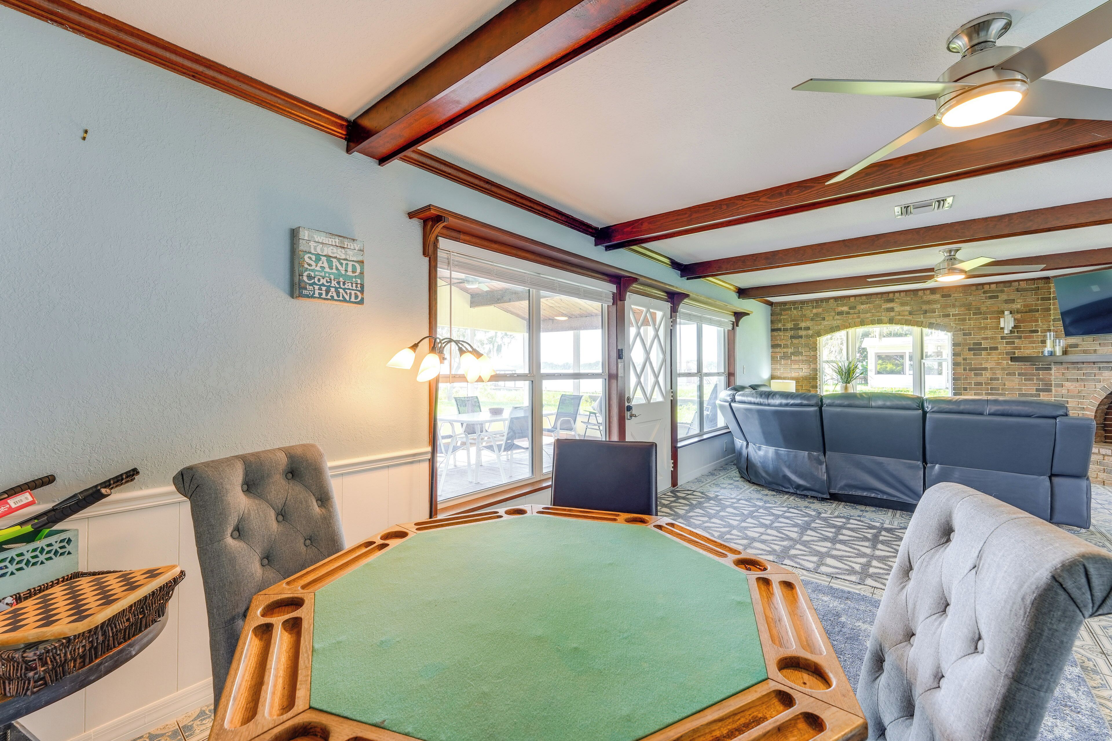 A pool table with a green felt surface, a tufted grey armchair, and a dark blue sofa in a room with wooden beams and a brick wall.