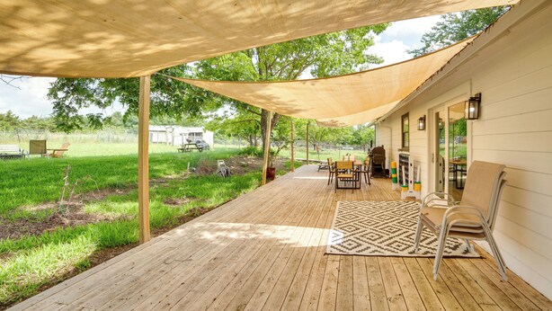 Een overdekt terras buiten, met houten vloeren, een getextureerd vloerkleed en tuinmeubilair.