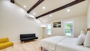 Een slaapkamer met een bed, een gele bank, een zwarte bank en twee ramen.