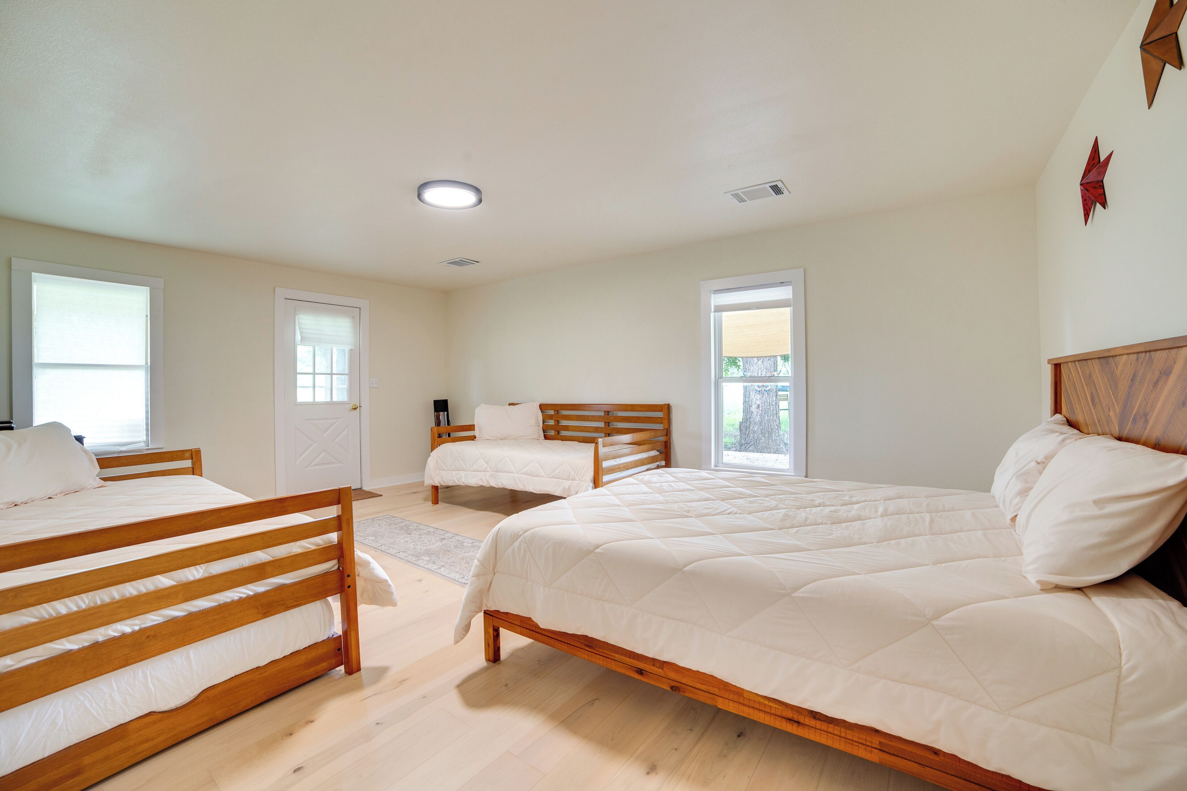 Une chambre à coucher avec trois lits en bois, du linge de lit blanc et de grandes fenêtres.
