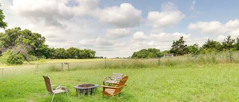 A grassy outdoor area with two wooden chairs and a small round table.