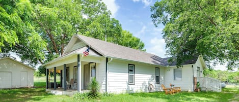 A white house with a porch, a flag, and a covered outdoor seating area.