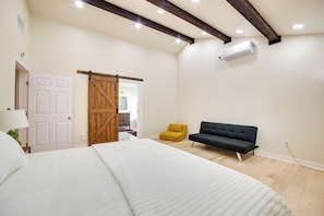 A bedroom with a bed, a sofa, a wooden door, and an air conditioning unit.