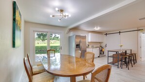 Een ruime keuken met witte kasten, een roestvrijstalen koelkast en een eetgedeelte met een houten tafel en rieten stoelen.