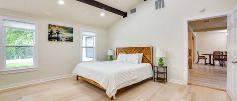 A bedroom with a wooden bed, a painting on the wall, and a view of the outdoors through a window.