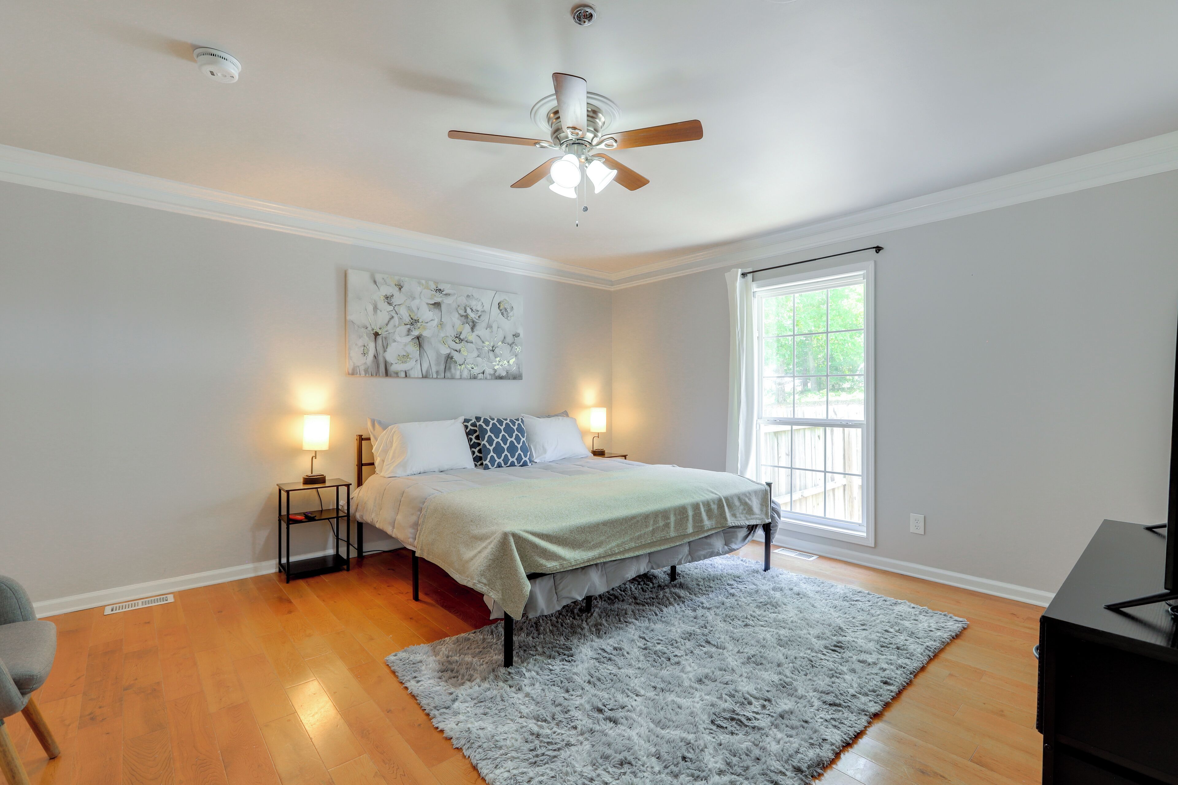 A bedroom with a bed, bedside lamps, a ceiling fan, a window, and a rug.