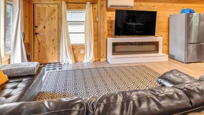A cozy living room with a leather sofa, patterned rug, wooden walls, a flat-screen TV, and a refrigerator.