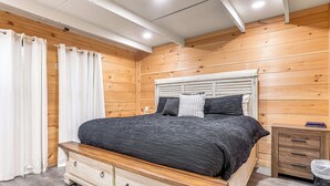 A bedroom with a wooden headboard, a bed with a dark bedspread, a nightstand, and a small wooden dresser with drawers.