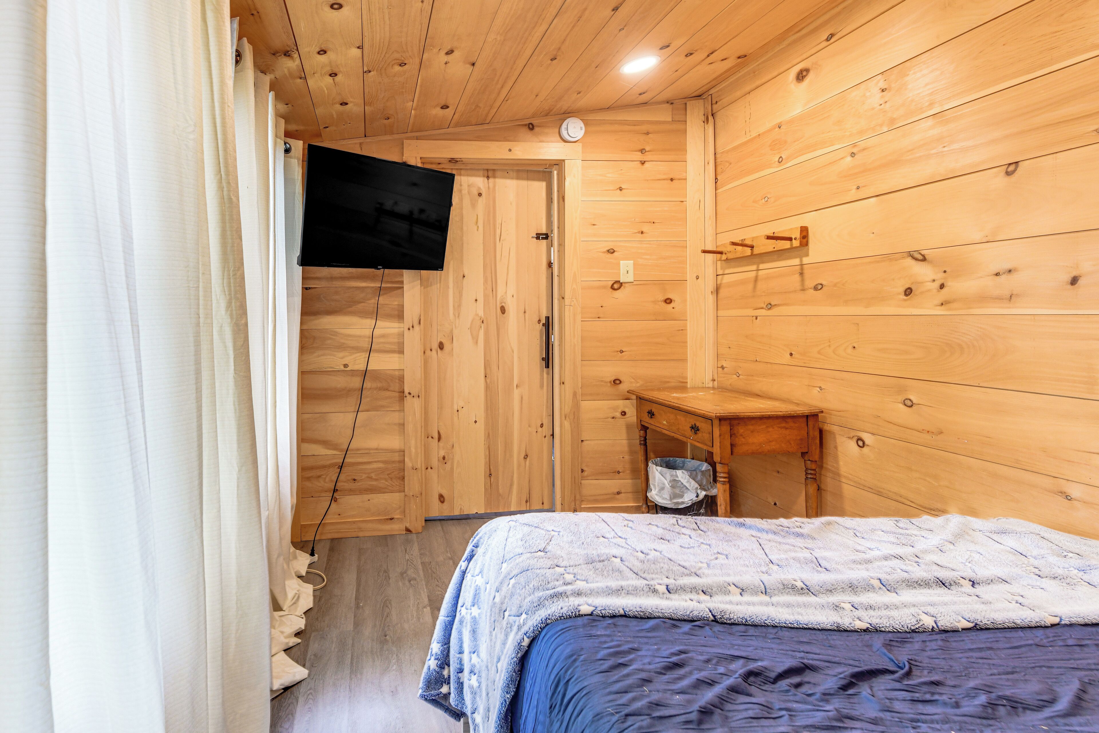 A wooden-paneled room with a bed, a small table, and a television mounted on the wall.