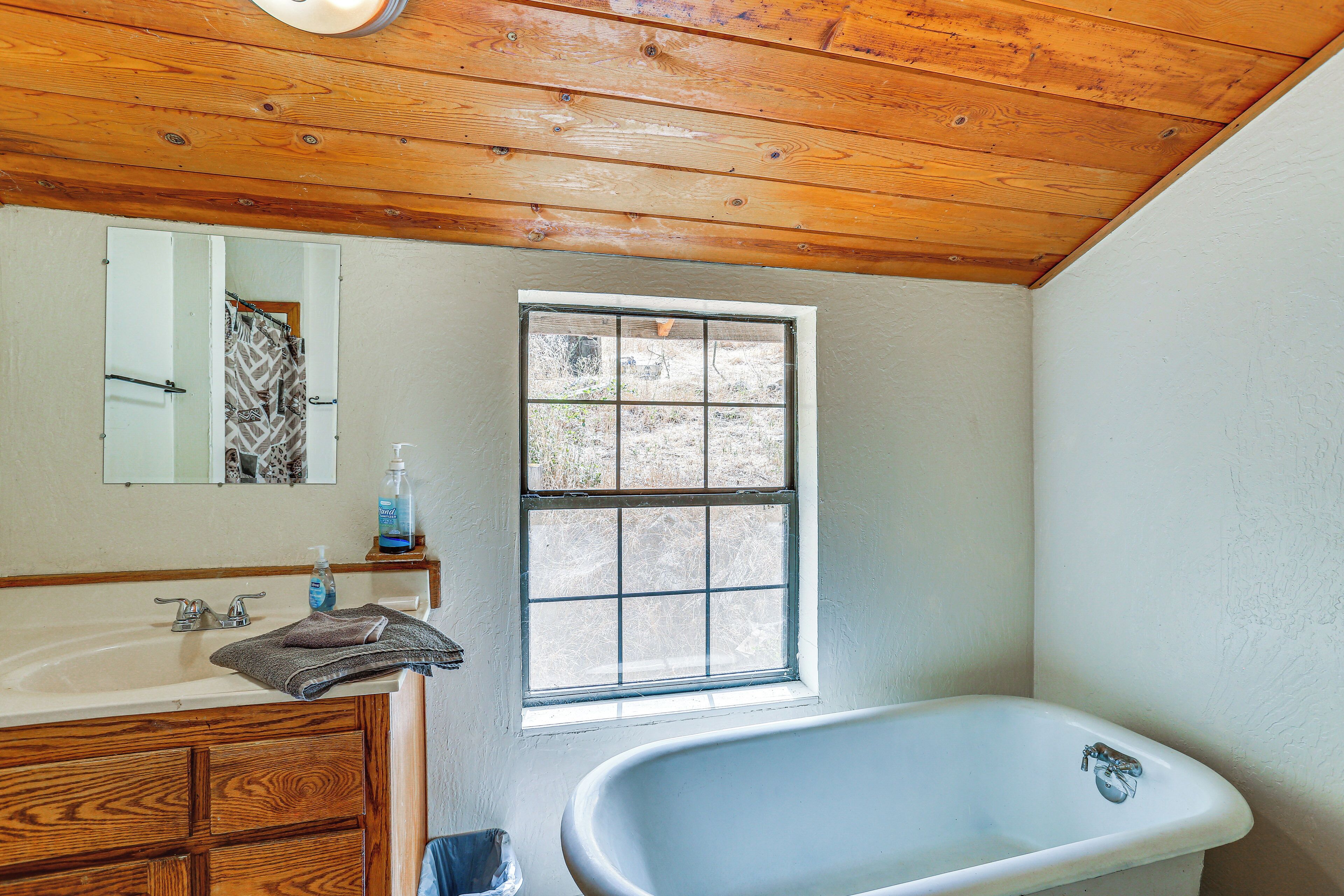 Un baño con techo de madera, una ventana, una bañera y un lavabo con espejo.