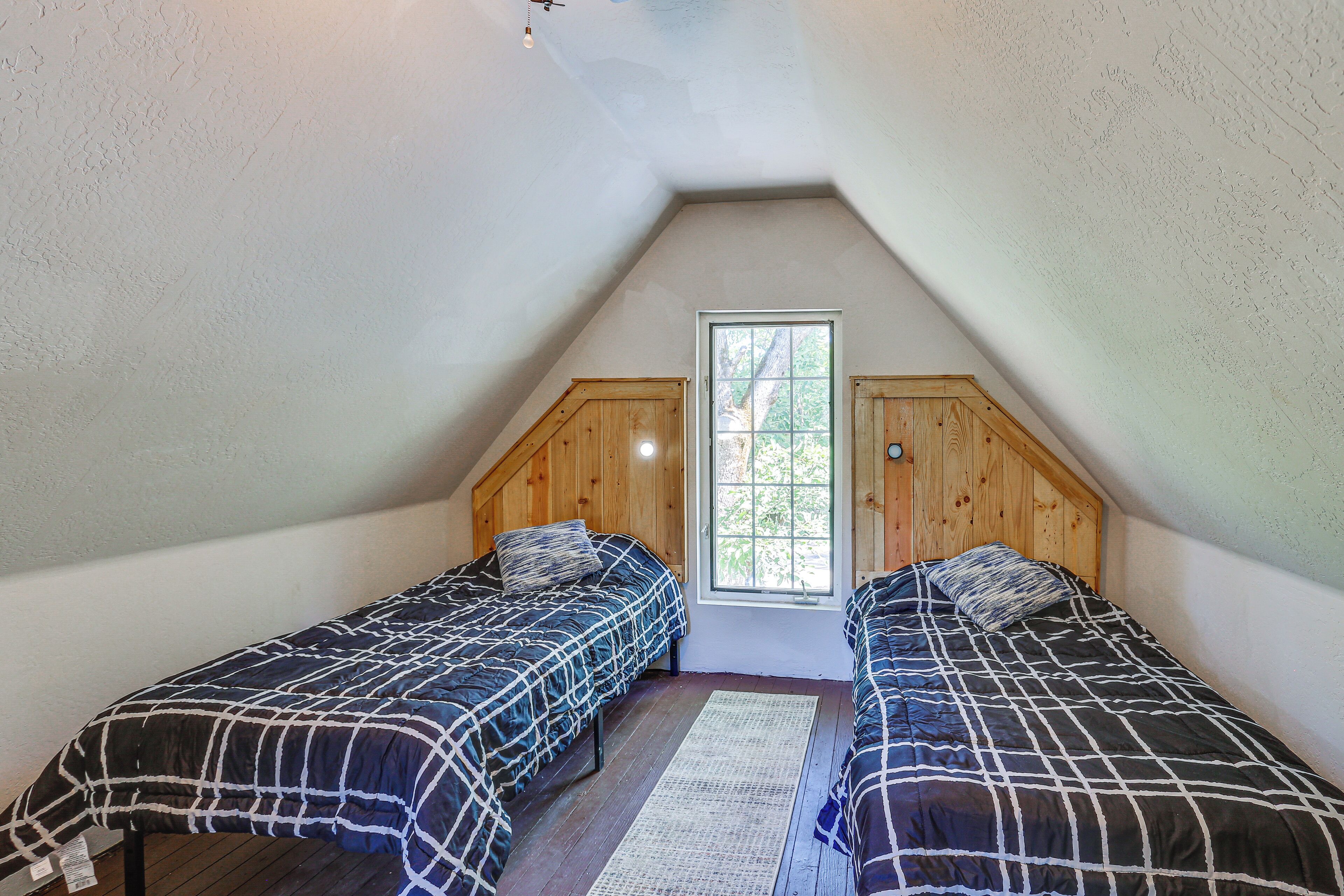 A small attic bedroom with two beds, wooden headboard, and a window.