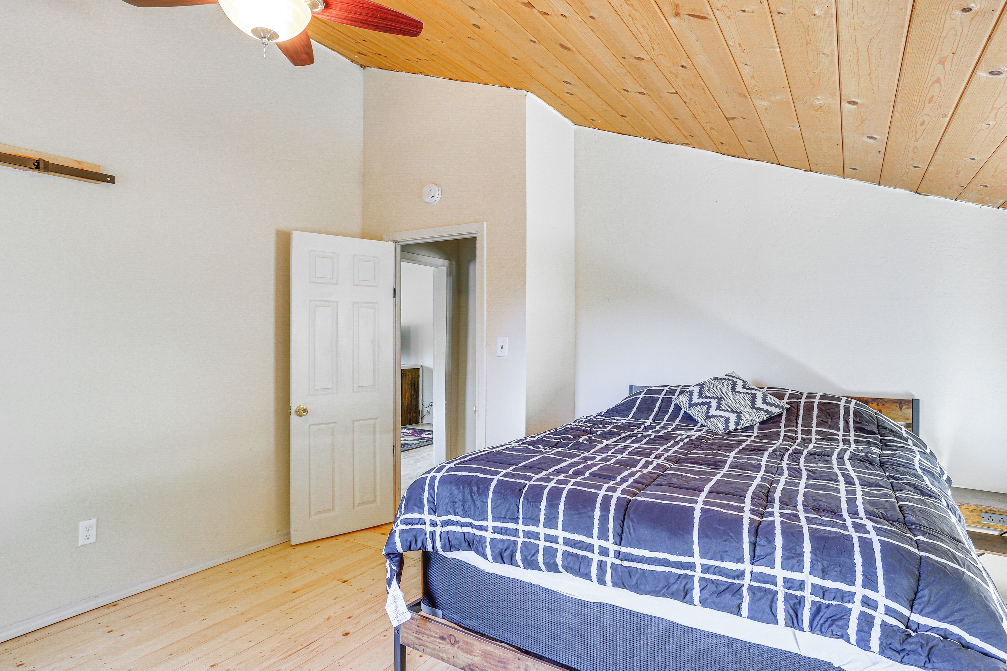 A bedroom with a wooden ceiling, a bed with a blue and white checkered bedspread, and a white door leading to another room.
