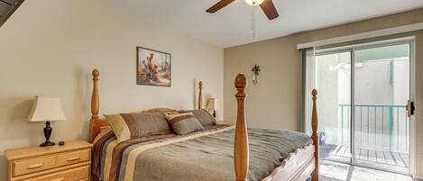 A bedroom with a bed, wooden nightstand, dresser, ceiling fan, and a sliding glass door to the outside.