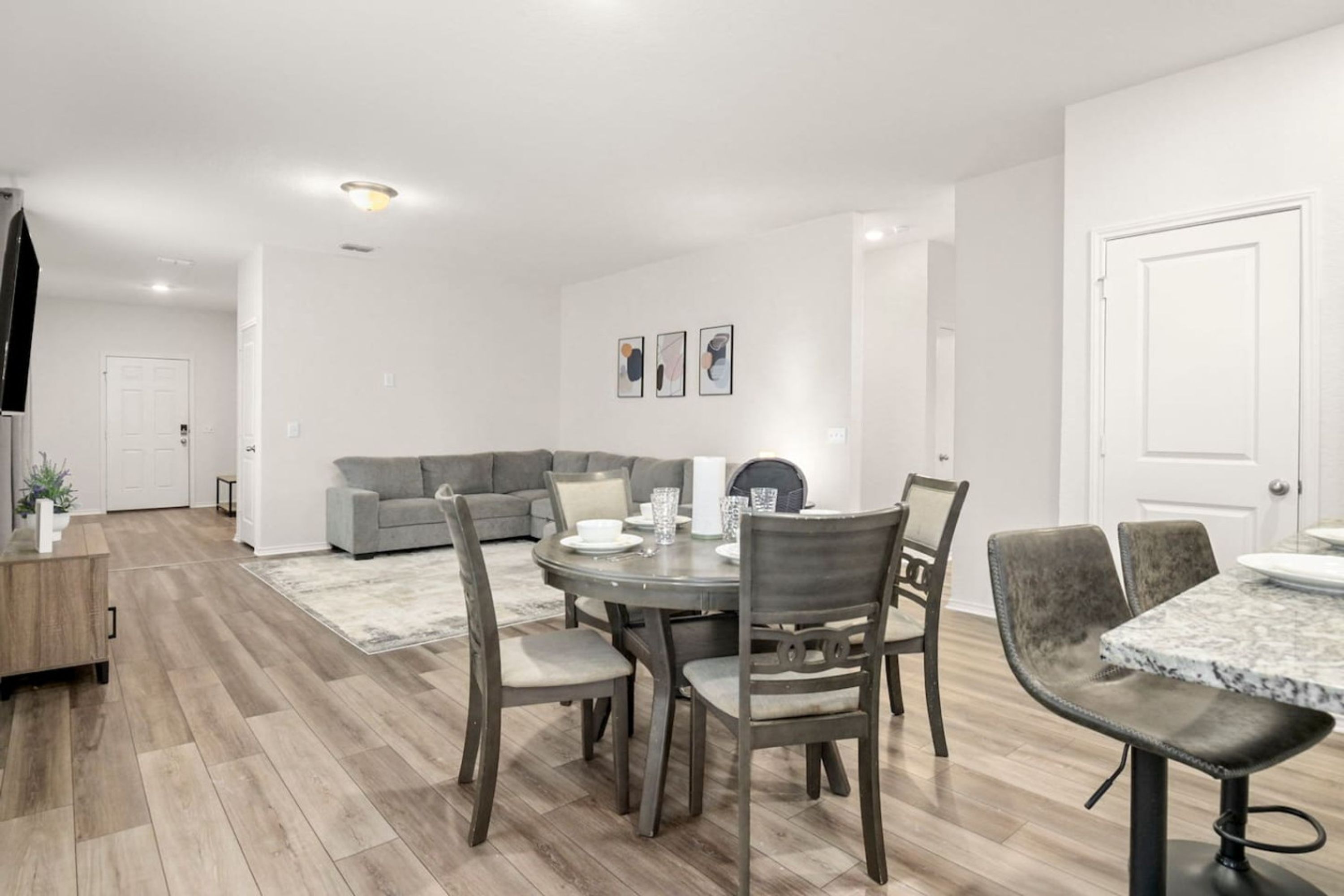 Ein modernes Wohnzimmer mit Essbereich, mit einem grauen Sofa, einem runden Esstisch mit Stühlen und Holzboden.