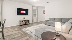 A modern living room with a grey sofa, a coffee table, a TV mounted on the wall, and a wooden cabinet. - Modern 3BR Home in San Antonio (San Antonio)