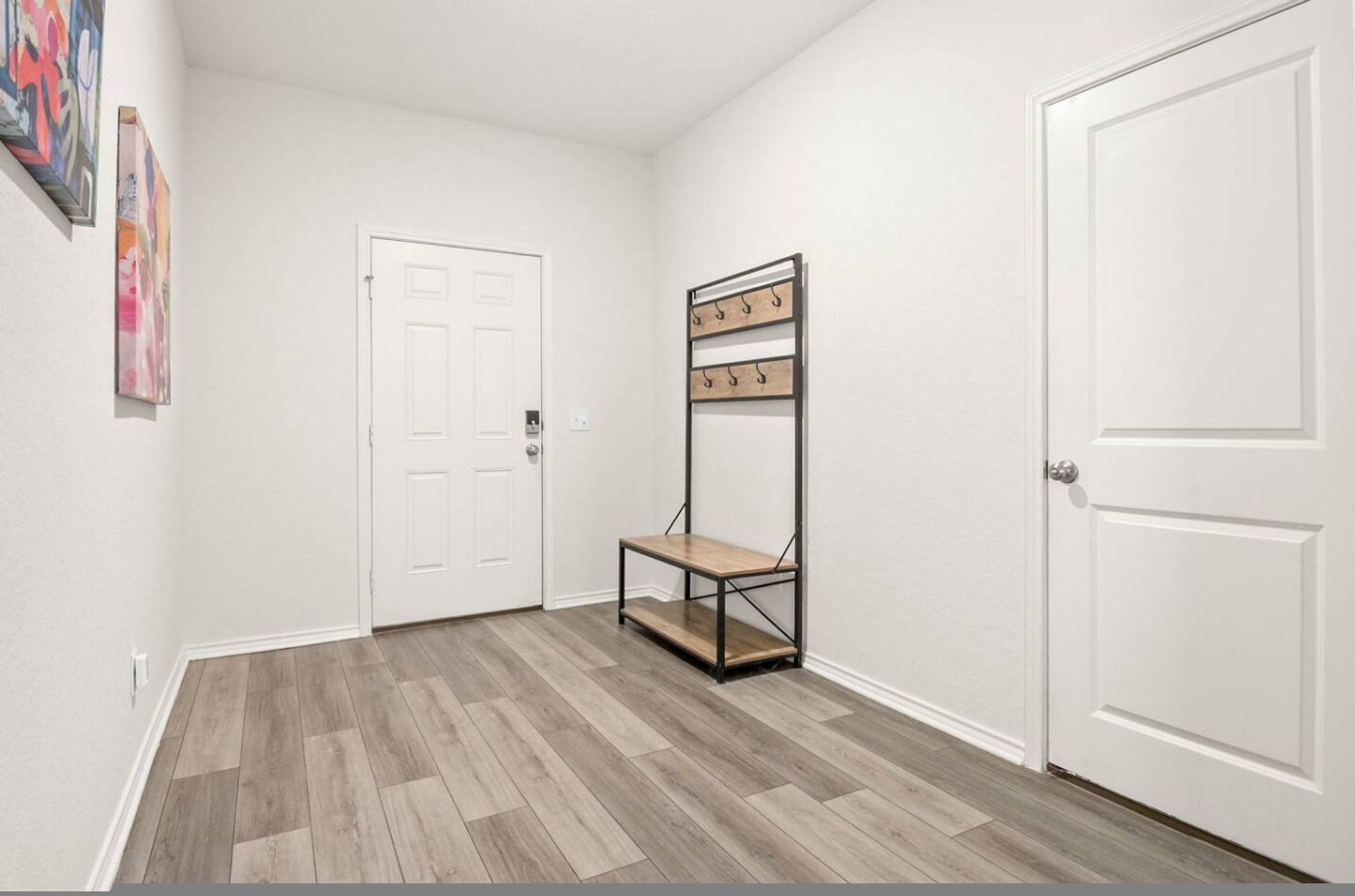 A hallway with a wooden floor, a white door, and a metal rack with hooks.