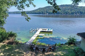 A dock extending into a lake with clear water, surrounded by greenery and a few chairs. - Lakefront A-Frame, Stunning Views, Private Dock (Merrimac)