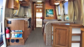 Interior de una autocaravana compacta con kitchenette, una cama y un baño.