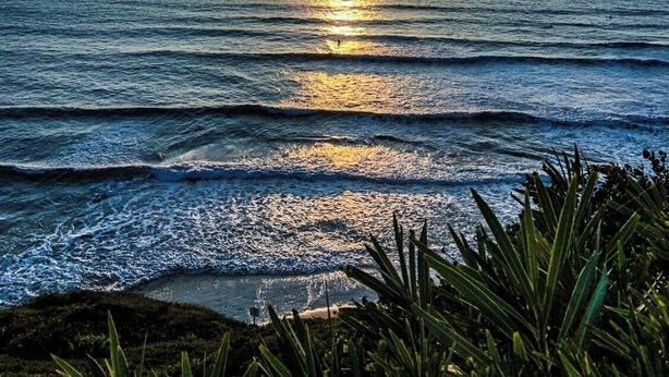 Atardecer sobre el océano con olas y cielo despejado.
