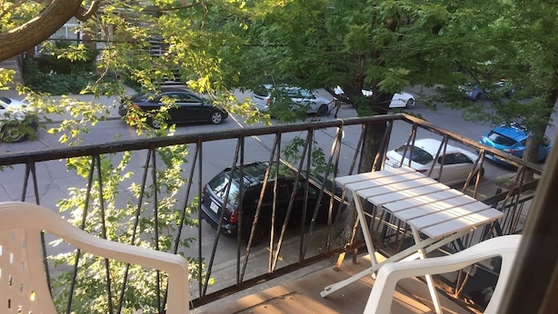 Un balcón con vista a coches estacionados y árboles.