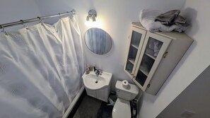 A bathroom with a shower curtain, a sink, a toilet, a mirror, and a cabinet with towels. - Simple, Clean,close to metro and groceries, marche atwater, canal lachine (Montréal)