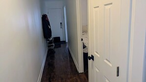 Un pasillo con suelo de madera, paredes blancas y un ventilador de techo. Hay puertas cerradas a la derecha y un perchero a la izquierda.