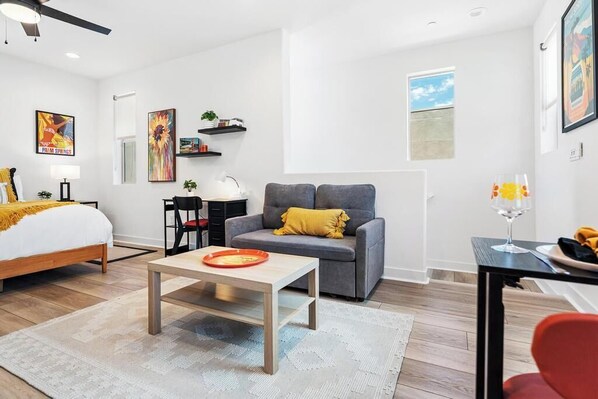 Una sala de estar moderna con cama, sofá gris y comedor con mesa y sillas.