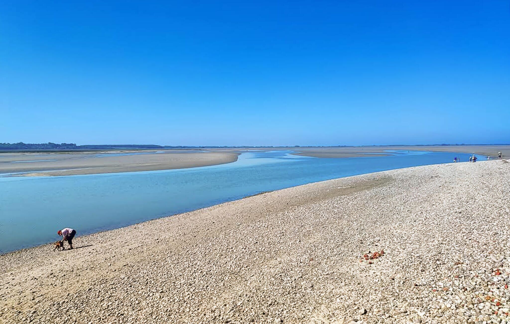 A pebbly beach with a calm water body and a clear sky.
