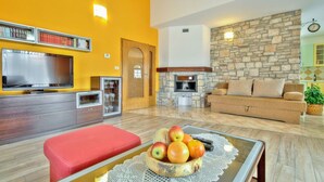 A living room with a red sofa, a wooden coffee table with fruit, a stone fireplace, and a television. - Villa Morena (Istria - Kaštel) (Kaštel)