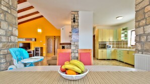 A kitchen with yellow cabinets, a stone wall, and a fruit bowl on the table. - Villa Morena (Istria - Kaštel) (Kaštel)