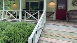 A covered porch with wooden steps, a red door, and a bench.
