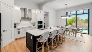 Une cuisine moderne avec des meubles blancs, un grand îlot central et un coin repas doté de chaises en osier.