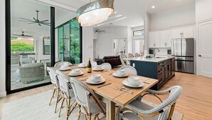 Une cuisine moderne avec des meubles blancs, un réfrigérateur en acier inoxydable et un coin repas comprenant une table en bois et des chaises en osier.