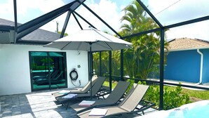 A rooftop pool area with lounge chairs, a hot tub, and a covered seating area with an umbrella.