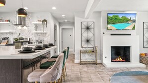 A modern kitchen with a central island, bar stools, a fireplace, and a TV mounted above it. - Mountain Views, Bocce Ball, and Poolside Bliss—PS Desert View Has It All! (Palm Springs)