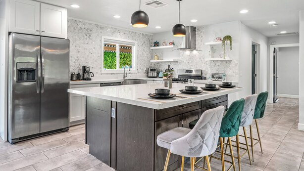 A modern kitchen with a large island, stainless steel appliances, pendant lighting, and a view of greenery outside. - Mountain Views, Bocce Ball, and Poolside Bliss—PS Desert View Has It All! (Palm Springs)