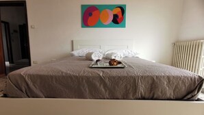 A neatly made bed with a beige quilt, a tray with a croissant and a glass of water, and a colorful abstract painting on the wall. - Spacious modern apartment, balcony with mountain view, free parking (Pescara)