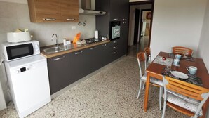 A compact kitchen with a microwave, stove, sink, and cabinets. There is a dining table with chairs and a small refrigerator. - Spacious modern apartment, balcony with mountain view, free parking (Pescara)