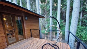 Eine Holzterrasse mit einem Hängesessel und einer Glastür, die zu einem Raum führt.