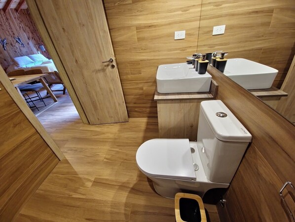 Un baño moderno con suelo de madera, inodoro blanco y lavamanos con espejo.