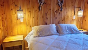 A wooden-paneled room with a bed, two wall-mounted lamps, and two wall-mounted bird decorations.
