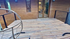 A wooden deck with a glass door leading to a room, a hammock, and a metal railing.