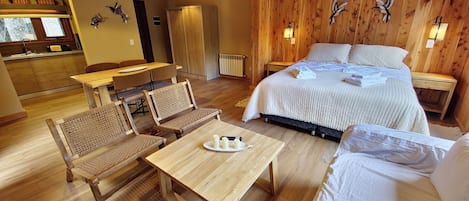 Una habitación acogedora con cama, una mesa de comedor y dos sillas. Se observa una zona de cocina al fondo.