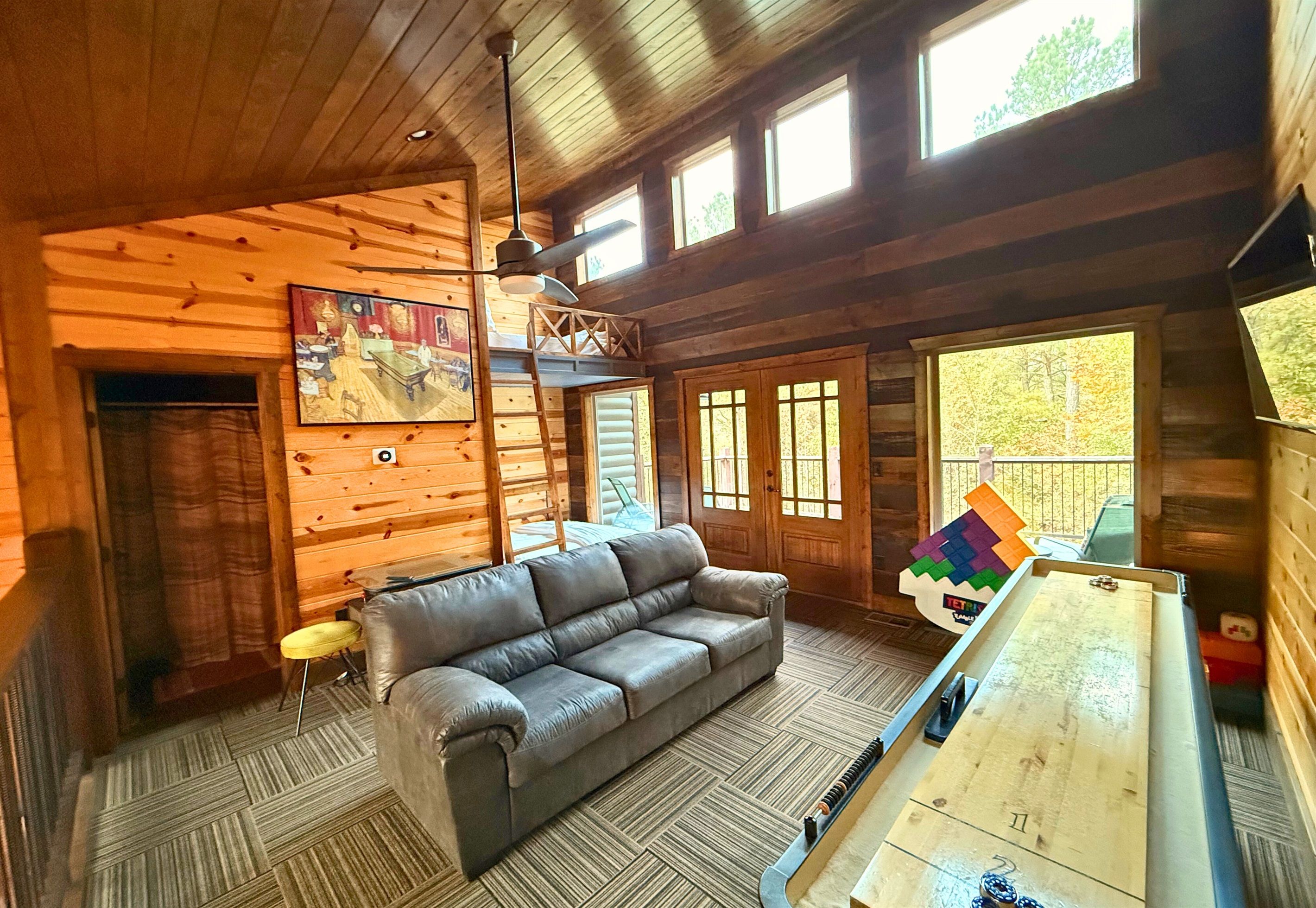 A log cabin interior with a sofa, a shuffleboard table, and large windows.