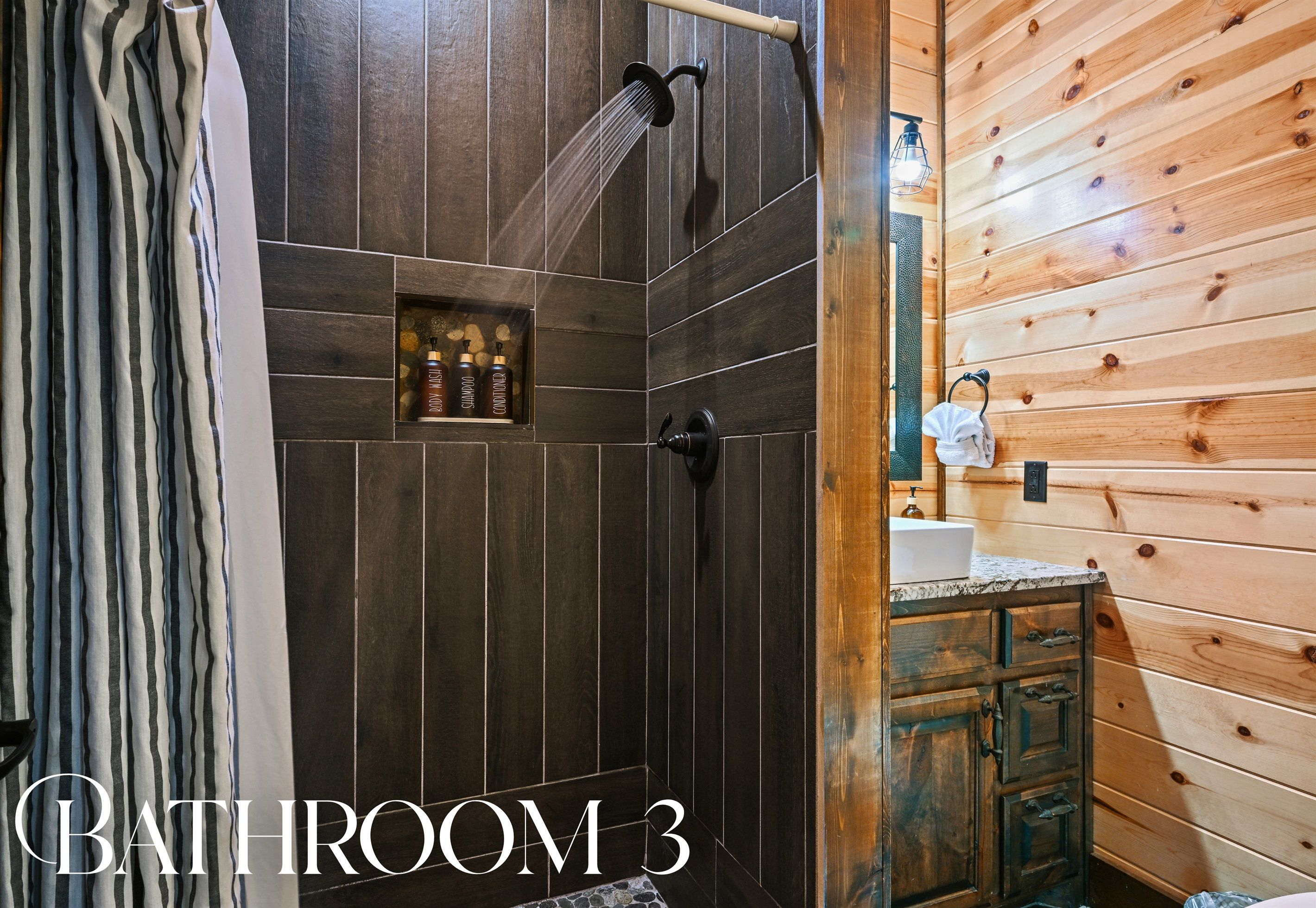 A bathroom with dark wooden walls, a shower with a handheld showerhead, and a shelf with toiletries.