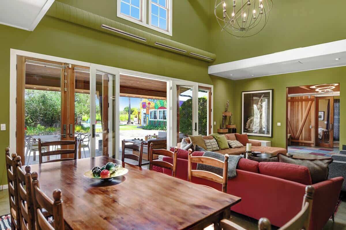 Amplia sala de estar con mesa de comedor de madera, sofá rojo y vistas al exterior.